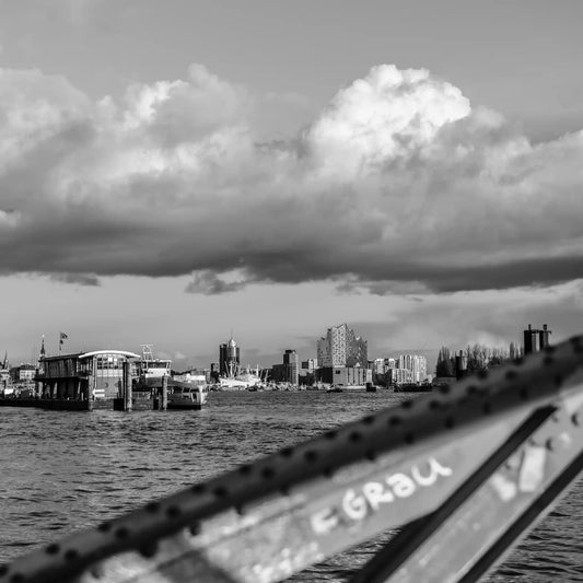 Schwarz weiß Foto über die Elbe, im Hintergrund die Elbphilharmonie und HTC, im Vordergrund ein unscharfer Brückenpfeiler
