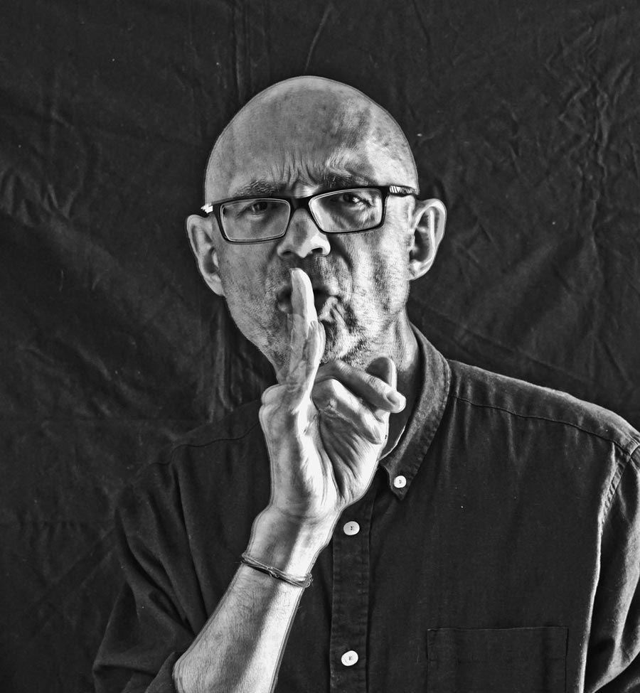 portrait Rolf Krieger, schwarz-weiß, hält einen Finger vor den Mund, Hintergrund schwarz, Kunst-Direkt.de