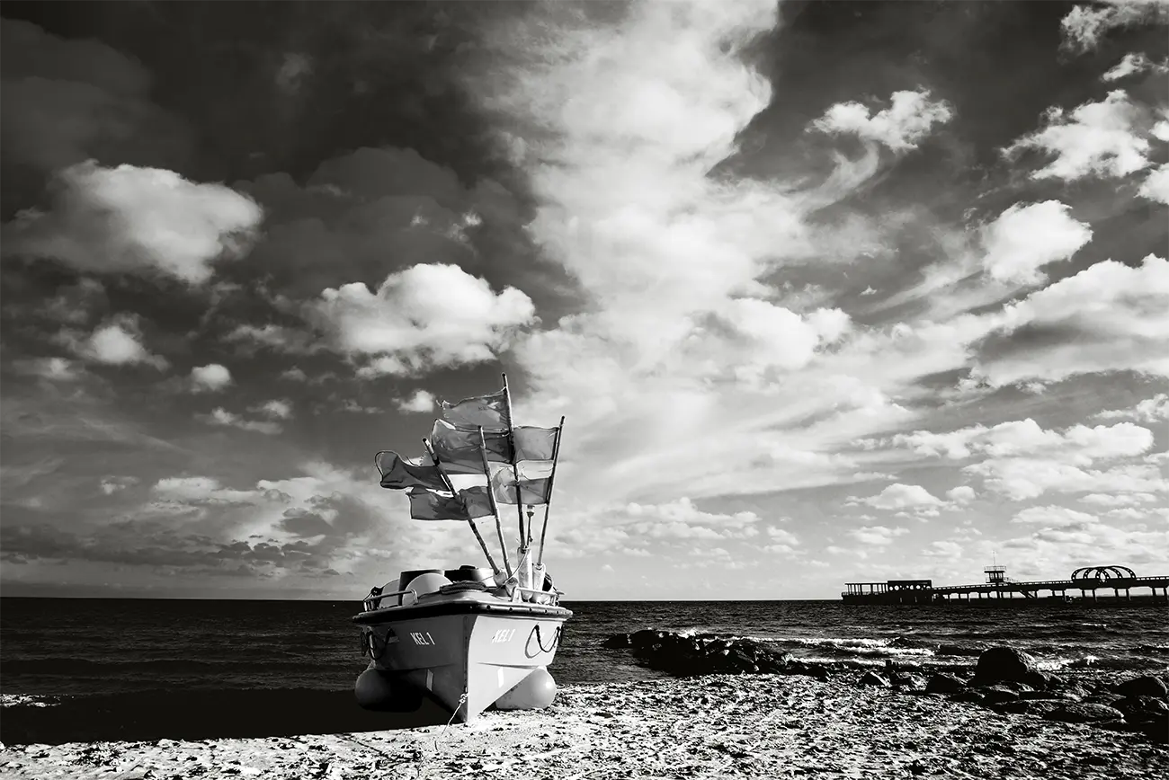 Kellenhusen – Fotokunst von Birte Zabel, Schwarz-Weiß-Fotografie, Fischerboot am Ostseestrand vor dramatischem Wolkenhimmel | Kunst-Direkt.de
